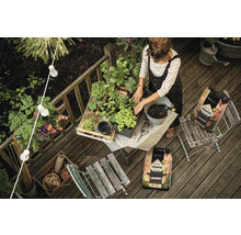 Žena sází rostliny do zeminy na dřevěném balkoně