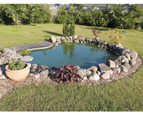 Zahradní jezírko s kamenným obrubníkem a dřevěným mostem v trávníku