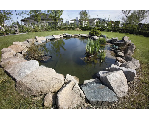 Kulaté zahradní jezírko obklopené kameny, zasazené do zelené zahrady.