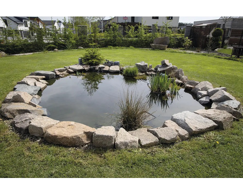 Zahradní jezírko s kamenným okrajem na trávníku.