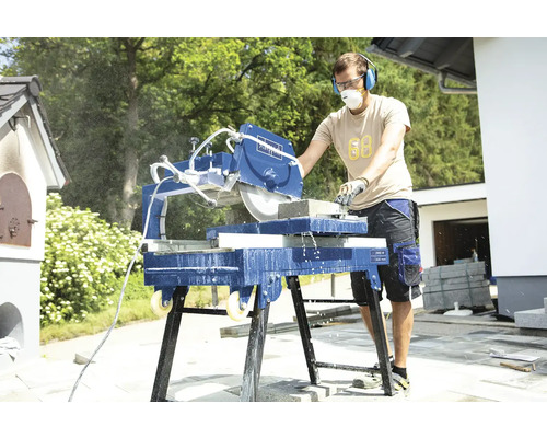 Muž používá venkovní pilu na kámen, vybavenou ochranou sluchu a protiprachovou maskou.