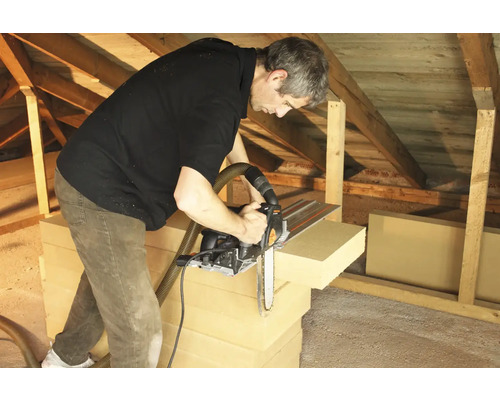 Muž řeže izolační desky řetězovou pilou v podkroví.