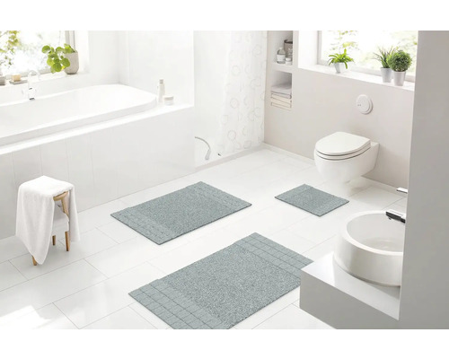 Světlá koupelna s vanou, umyvadlem, toaletou a třemi šedými koupelnovými koberci