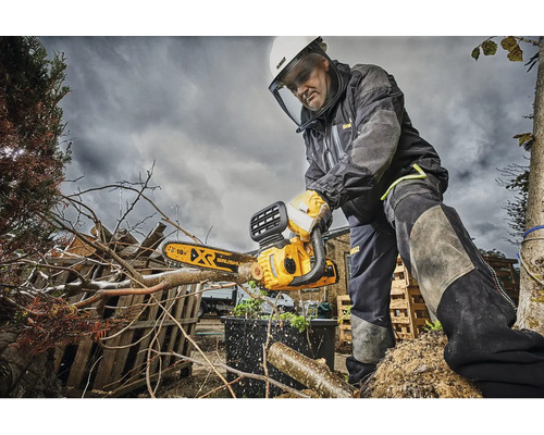 Muž s ochrannými pomůckami používá řetězovou pilu DeWalt k prořezávání větví.