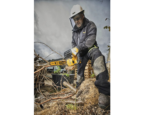 Muž s ochrannou přilbou a obličejovým štítem řeže větvě motorovou pilou.