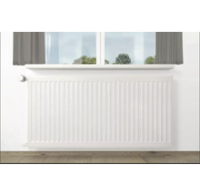 Bílý radiátor pod oknem v místnosti.