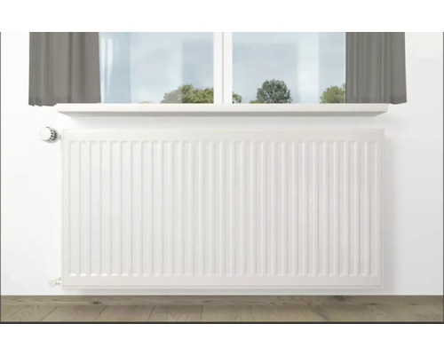 Bílý radiátor pod oknem v místnosti.