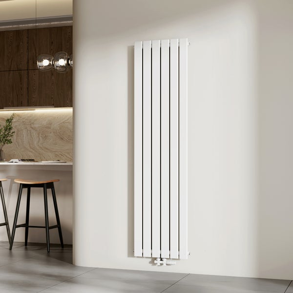 Bílý vertikální designový radiátor v moderním interiéru s navazující kuchyní, dřevěnými skříňkami a barovými stoličkami.