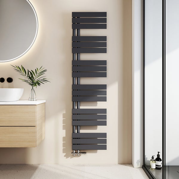 Moderní designový koupelnový radiátor v antracitové barvě s plochými lamelami, instalovaný v světlé koupelně vedle dřevěné skříňky.