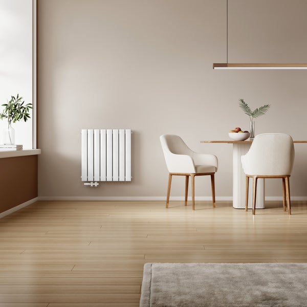 Moderní designový radiátor namontovaný na stěně ve světlé jídelně se dřevěným stolem, židlemi a dřevěnou podlahou.