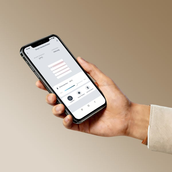 Ruka drží chytrý telefon s aplikací pro ovládání chytrého sušáku na ručníky s regulací teploty.
