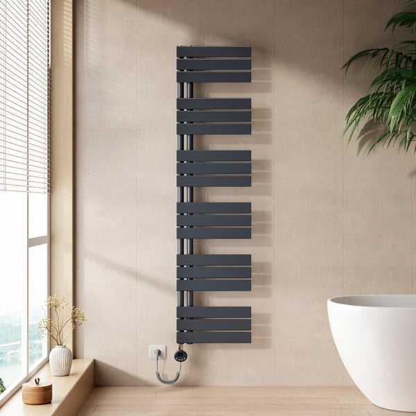 Moderni elektricky koupelnovy radiator v antracitove barve na svetle dlazdene stene v koupelne vedle bile vany.