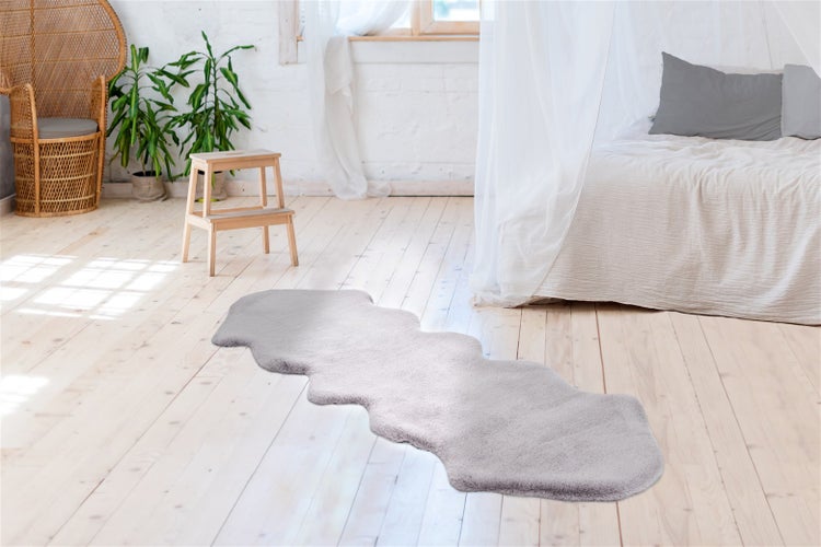 Dlouhý, huňatý koberec z umělé kožešiny na světlé dřevěné podlaze ve světlé ložnici s postelí a rostlinami.