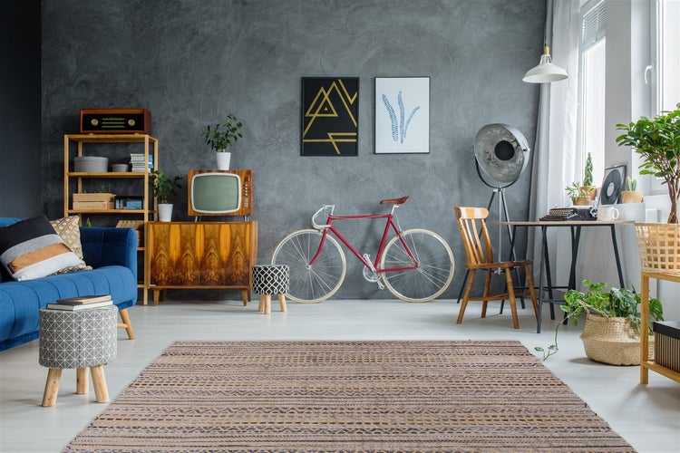 Moderní obývací pokoj s šedou strukturovanou stěnou, retro nábytkem, červeným kolem, modrou pohovkou, vzorovaným kobercem a průmyslovým osvětlením.