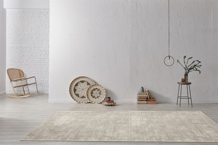 Moderní obývací pokoj s béžovým texturovaným kobercem, bílými stěnami, houpacím křeslem a minimalistickou dekorací ve světlé atmosféře.