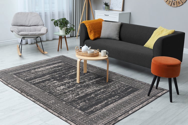 Moderní obývací pokoj s tmavě šedým kobercem v pouŸitém vzhledu s meandrovým okrajem na světlé podlaze, s pohovkou, houpacím křeslem a stoličkou.