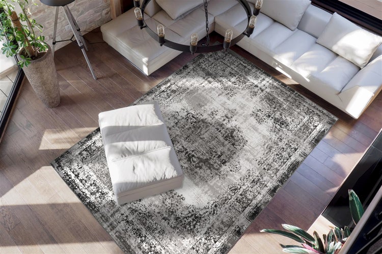 Světlý moderní obývací pokoj s bílou koženou pohovkou a obdélníkovým kobercem s šedo-černým vintage vzorem na tmavé dřevěné podlaze.