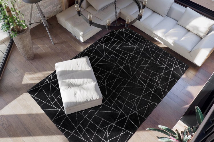 Moderní černý koberec s bílým geometrickým vzorem čar ve světlém obývacím pokoji s bílou pohovkou a dřevěnou podlahou.