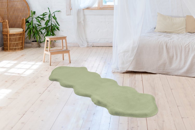 Podlouhlý, vlnitý koberec s měkkým vzhledem na světlé dřevěné podlaze ve světlé ložnici s postelí a proutěným křeslem.