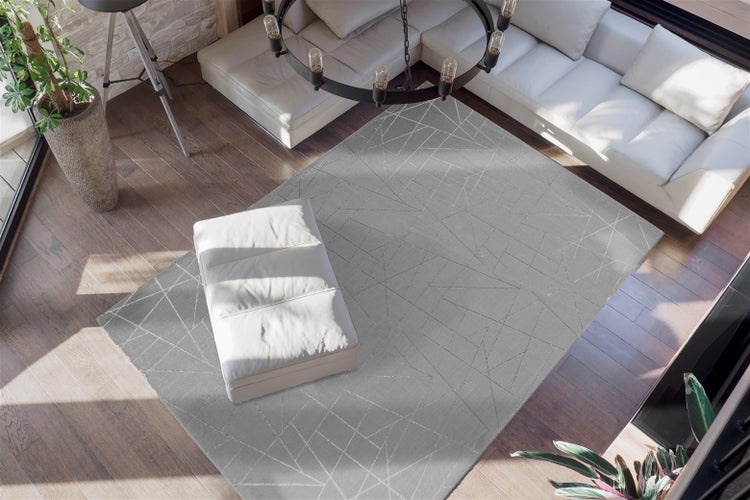 Moderní světlý obývací pokoj s šedým kobercem s geometrickým vzorem na tmavé dřevěné podlaze, s bílou pohovkou a taburetem.