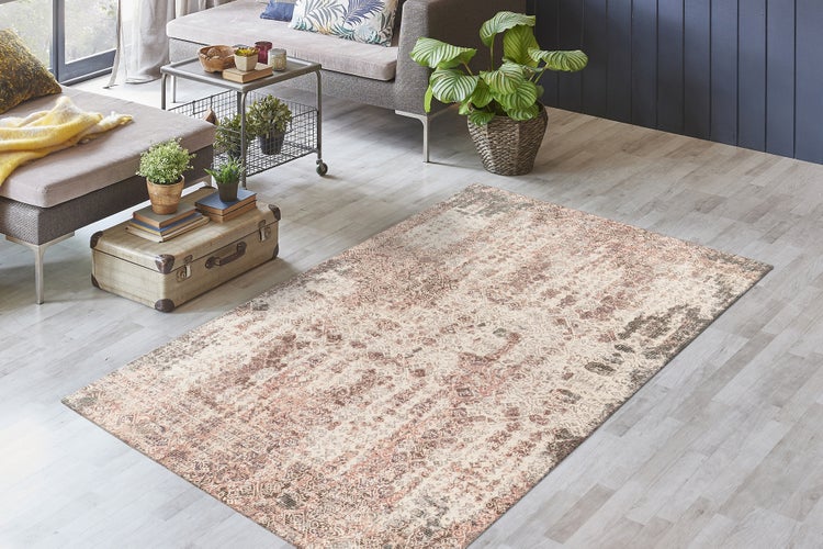Obdélníkový koberec s orientálním vintage vzorem ve světlém obývacím pokoji na šedé podlaze vedle pohovky a rostlin.