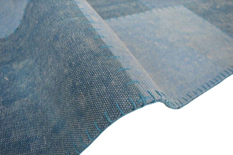 Detail modrého tkaného koberce v patchworkovém designu s viditelným ozdobným prošíváním.