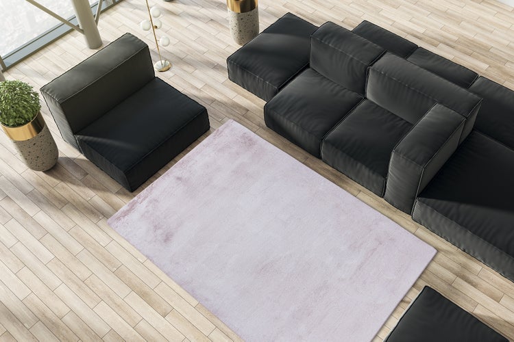Moderní obývací pokoj se světle růžovým kobercem na světlé dřevěné podlaze, doplněný černou modulární pohovkou a křeslem.