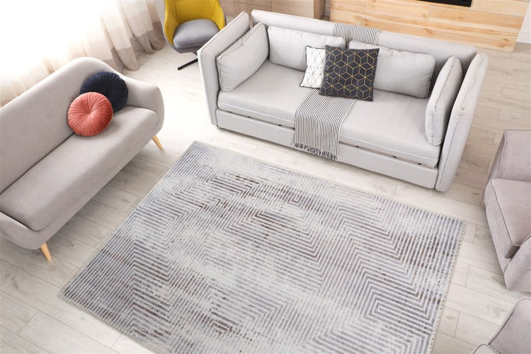 Světlý moderní obývací pokoj s obdélníkovým kobercem s geometrickým klikatým vzorem na světlé dřevěné podlaze, obklopený šedými pohovkami.