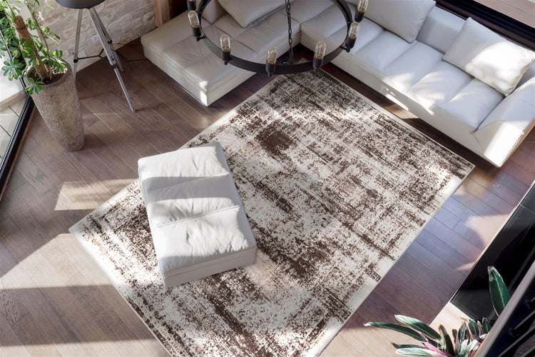 Obdélníkový koberec s abstraktním vintage vzorem v hnědé a krémové barvě v moderním obývacím pokoji na dřevěné podlaze pod bílou pohovkou.