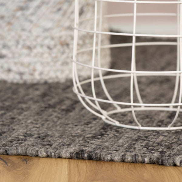Detailní pohled na šedý vlněný koberec se strukturou na dřevěné podlaze, s bílým drátěným košem.