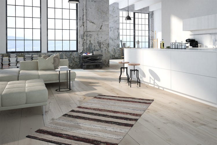 Světlý industriální loft s otevřenou kuchyní a obývacím pokojem, světlou dřevěnou podlahou, bílým ostrůvkem a velkými okny.