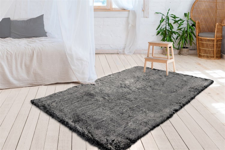 Šedý koberec s vysokým vlasem ve vzhledu umělé kožešiny na světlé dřevěné podlaze ve světlé ložnici s postelí a rostlinami.