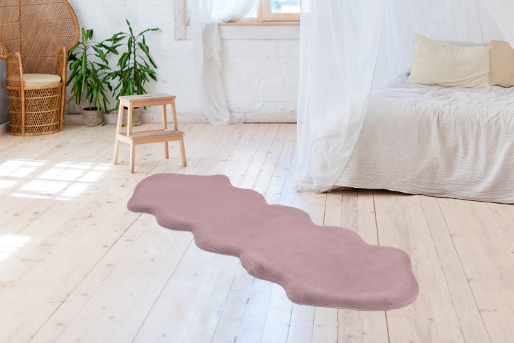 Podlouhlý, vlnitý koberec z umělé kožešiny ve světlé ložnici s dřevěnou podlahou, postelí a pokojovými rostlinami.
