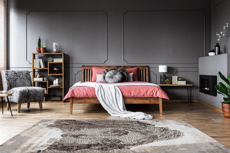 Moderní ložnice s dřevěnou postelí, tmavými nástěnnými panely, vzorovaným křeslem a velkým kobercem na světlé dřevěné podlaze.