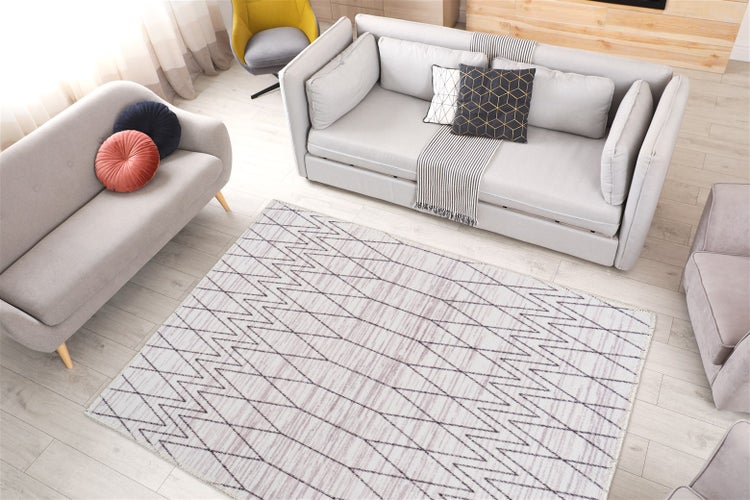 Moderní obývací pokoj se světlou pohovkou, dvoumístným sedadlem a velkým kobercem s geometrickým cikcak vzorem na světlé podlaze.