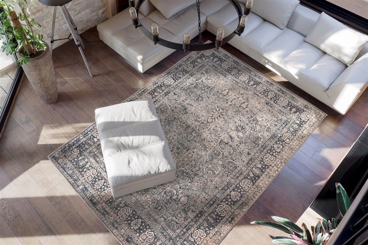 Světlý obývací pokoj s velkým orientálním kobercem ve vintage stylu na dřevěné podlaze, bílou koženou pohovkou, taburetem a moderním lustrem.