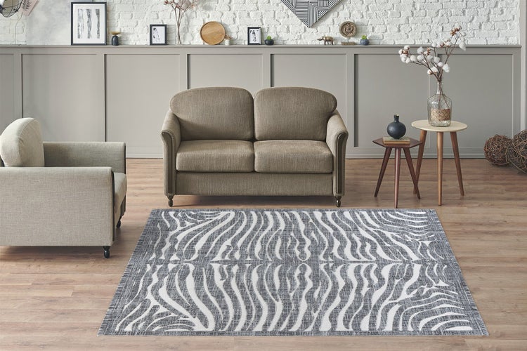 Moderní obývací pokoj s vzorovaným kobercem se zebřím designem před pohovkou a křeslem na dřevěné podlaze.