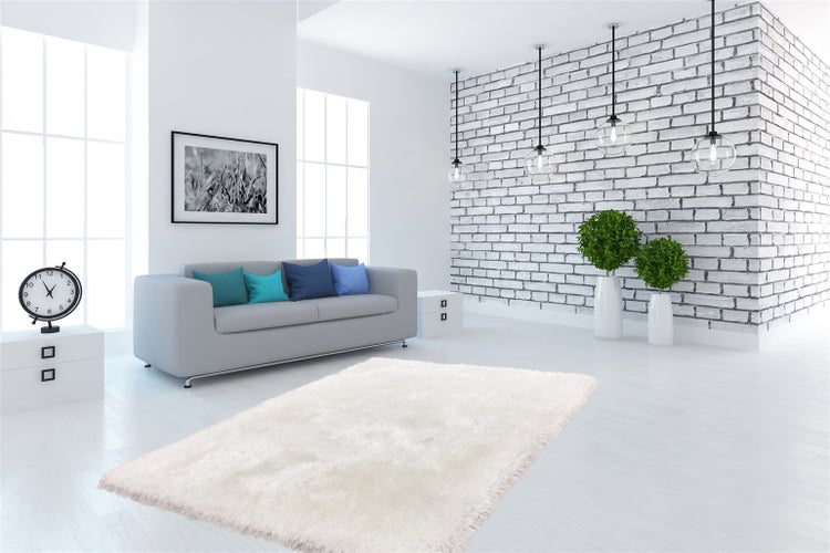 Světlý obývací pokoj s bílým kobercem s vysokým vlasem, šedou pohovkou, bílou cihlovou stěnou a velkými okny. Moderní design.