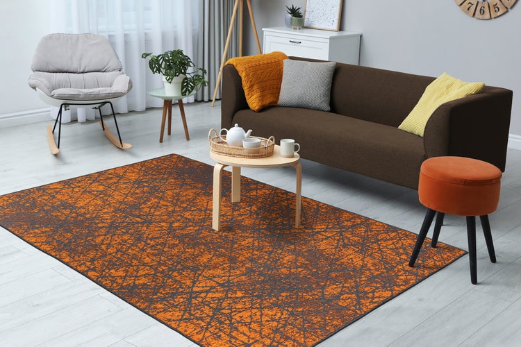 Moderní obývací pokoj s oranžovo-šedým kobercem, hnědou pohovkou, dřevěným stolkem, šedým houpacím křeslem a oranžovým taburetem. Světlý a uspořádaný.