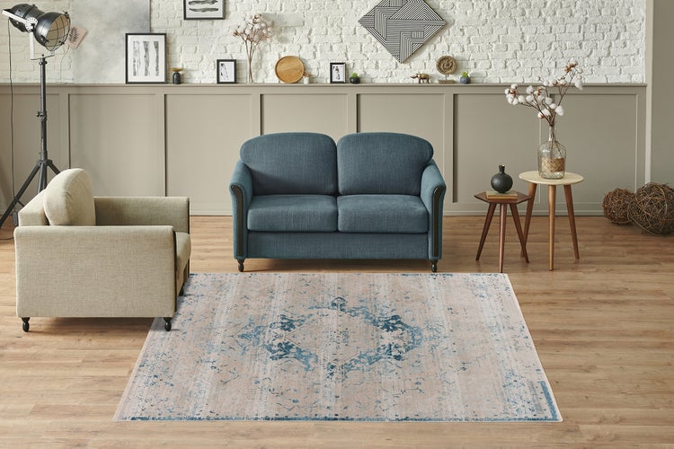 Obývací pokoj s modro-béžovým vintage kobercem na dřevěné podlaze, modrou pohovkou a béžovým křeslem u bílé cihlové stěny.