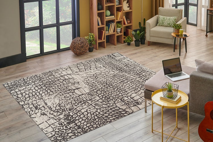 Obdélníkový koberec s šedo-bílým zvířecím vzorem ve světlém obývacím pokoji s dřevěnou knihovnou a křeslem na laminátové podlaze.