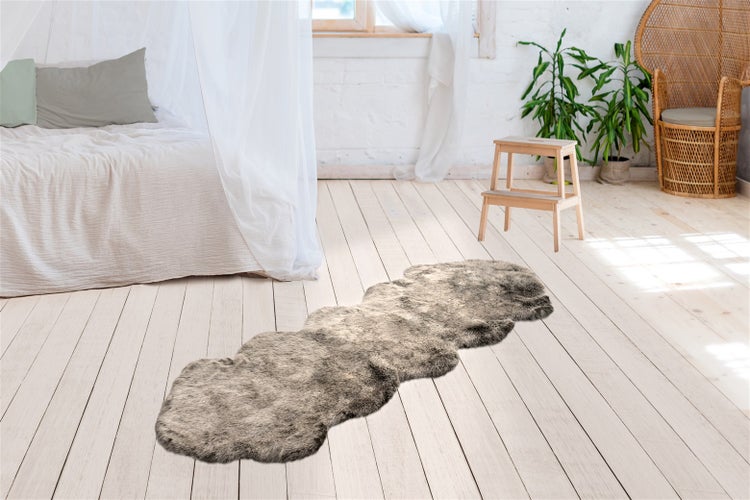 Koberec s vysokým vlasem v imitaci kožešiny na světlé dřevěné podlaze ve světlé ložnici s postelí a rostlinami.
