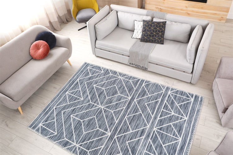 Moderní obývací pokoj s kobercem s geometrickým vzorem na světlé dřevěné podlaze, světle šedými pohovkami a dekoračními polštáři.