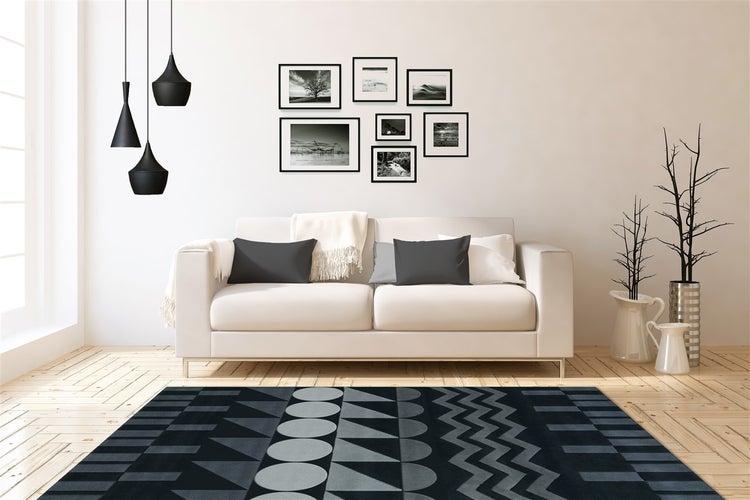 Světlý obývací pokoj s pohovkou, dřevěnou podlahou, černošedým kobercem s geometrickým vzorem, galerií na stěně a černými závěsnými svítidly.