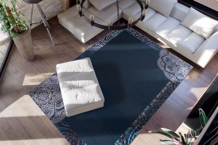 Tmavě modrý koberec s mandalovým vzorem na dřevěné podlaze, kombinovaný s bílou pohovkou a taburetem ve světlém, moderním obývacím pokoji.