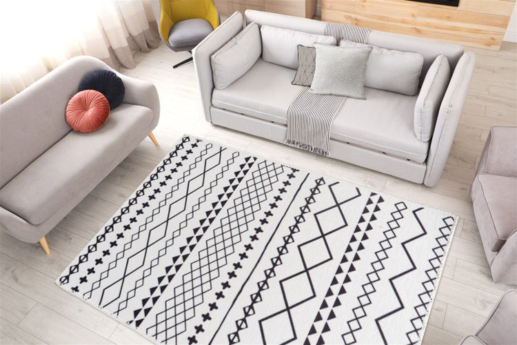 Světlý, moderně zařízený obývací pokoj s šedými pohovkami a černo-bílým kobercem s geometrickým vzorem na světlé dřevěné podlaze.