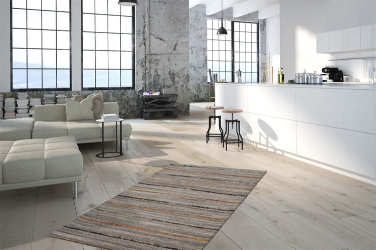 Světlý loft v industriálním stylu se světlou podlahou, bílou kuchyní a moderním obývacím prostorem se sedačkou a kobercem.