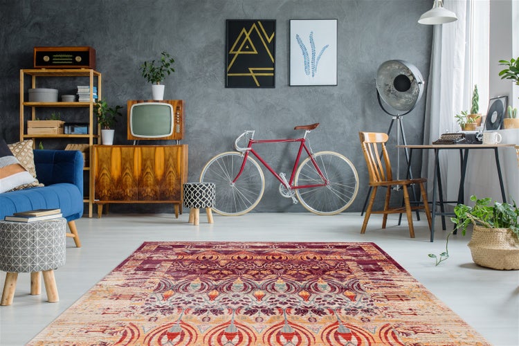 Světlý obývací pokoj v retro stylu s barevným orientálním kobercem, modrou pohovkou, vintage dřevěným nábytkem, kolem u šedé stěny a světlou podlahou.