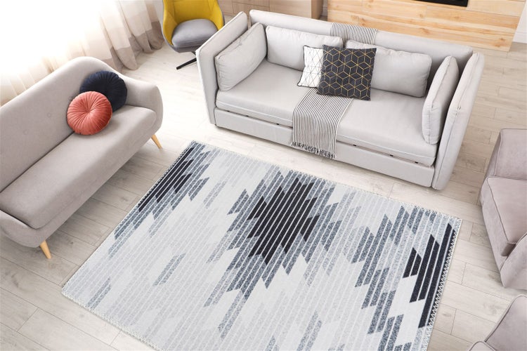 Moderní obývací pokoj s kobercem s geometrickým vzorem v šedé a černé barvě na světlé dřevěné podlaze se šedými pohovkami.