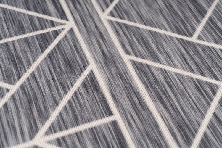 Detailní záběr na tkaný koberec s geometrickým vzorem linií a strukturovaným povrchem.